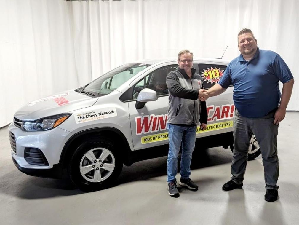 Winner's car in the background as two people shake hands