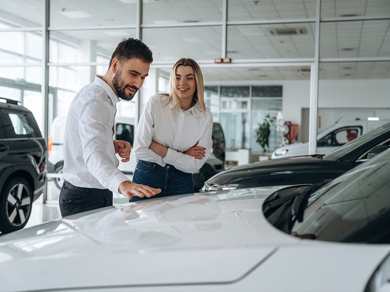 Two people examining cars in a showroom.