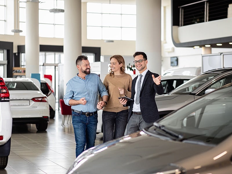 Salesman guiding couple through car options.